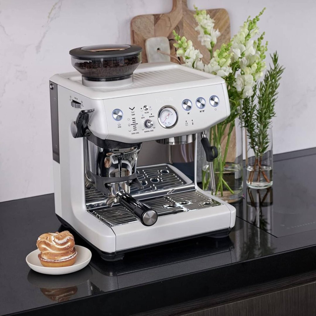 White Breville coffee machine on a black countertop with flowers and a pastry