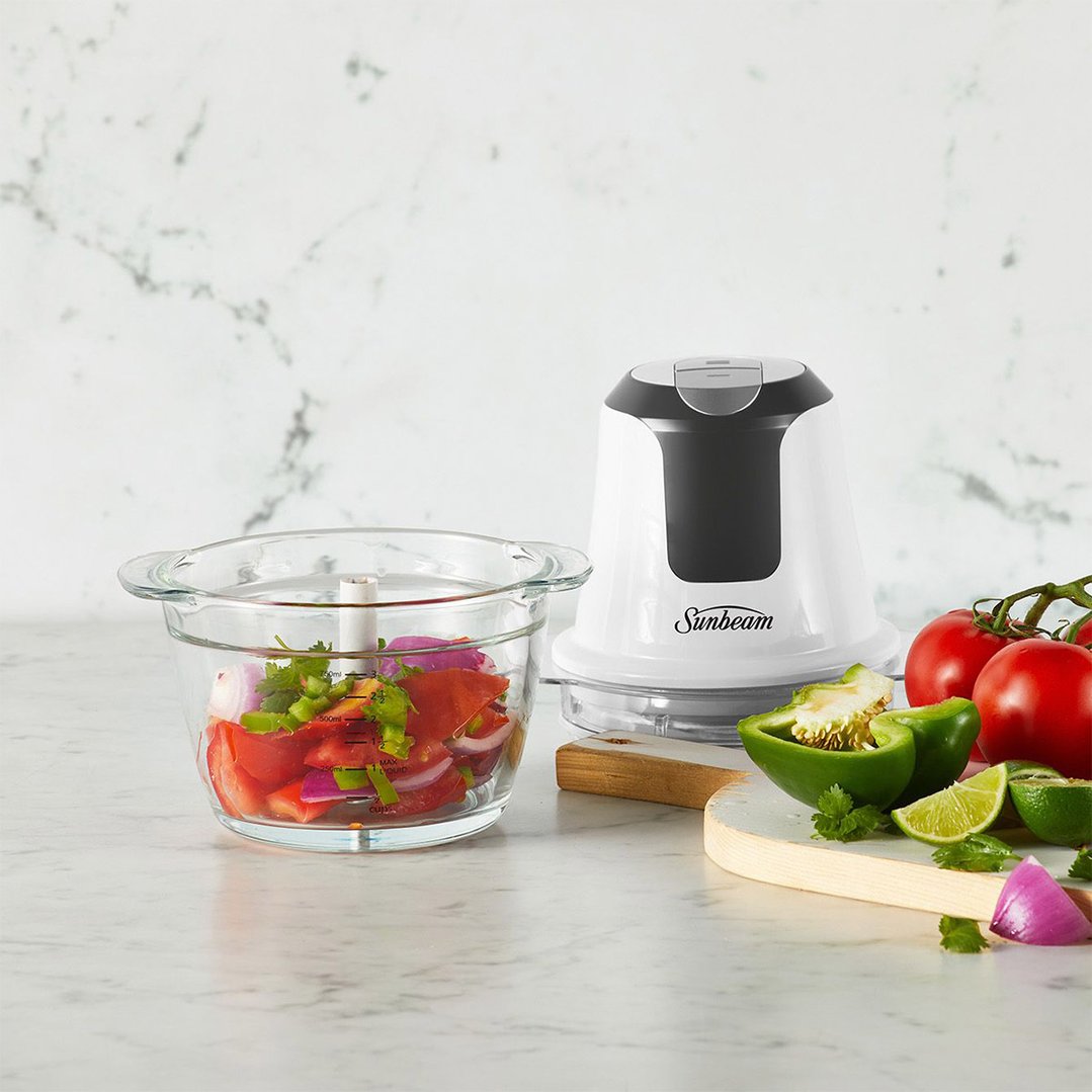 Sunbeam food processor with chopped vegetables in a glass bowl on a marble counter