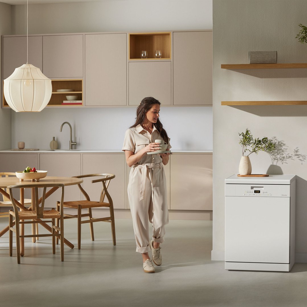 Woman holding dishes in a modern kitchen with a freestanding dishwasher