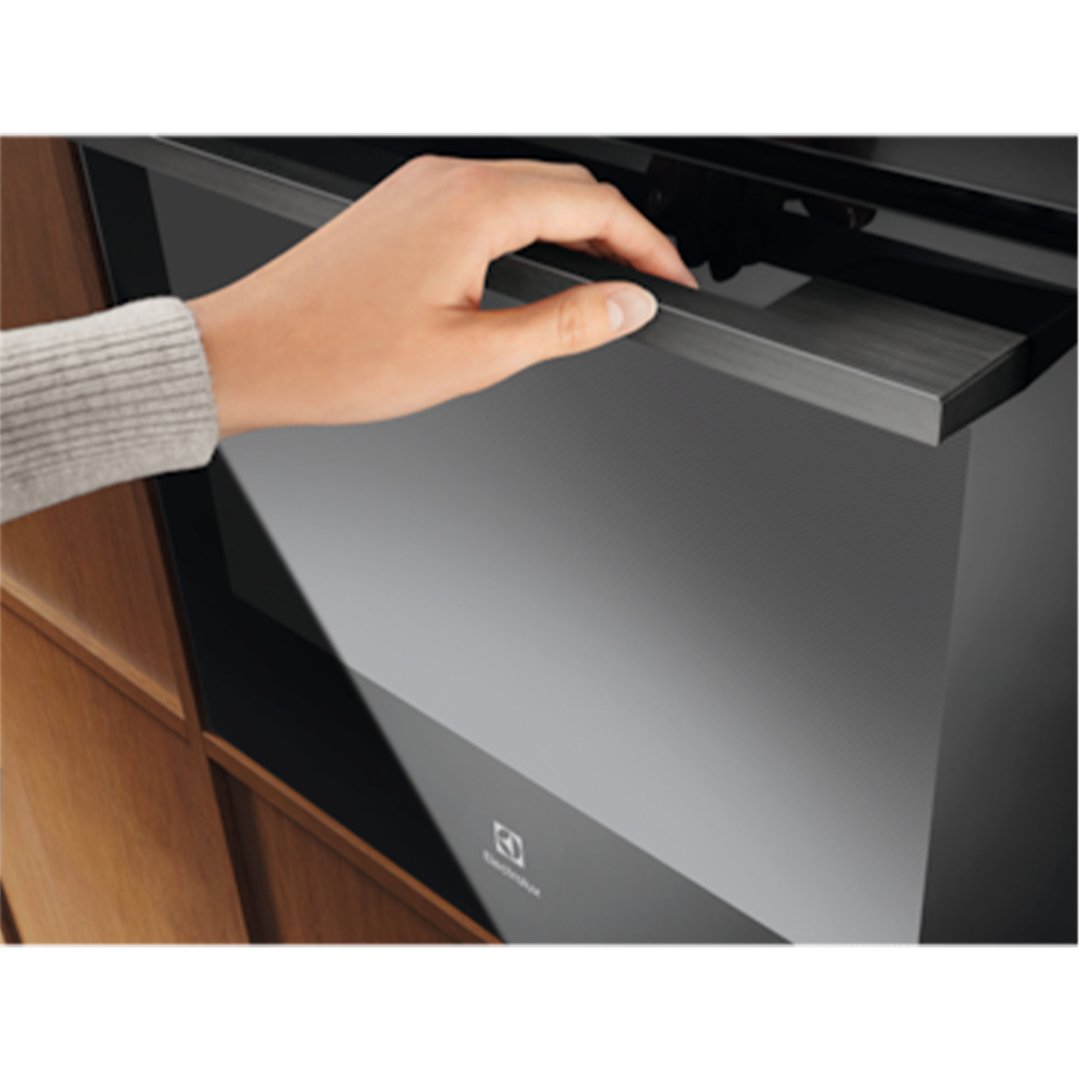 Hand opening the door of a black built-in oven in a kitchen