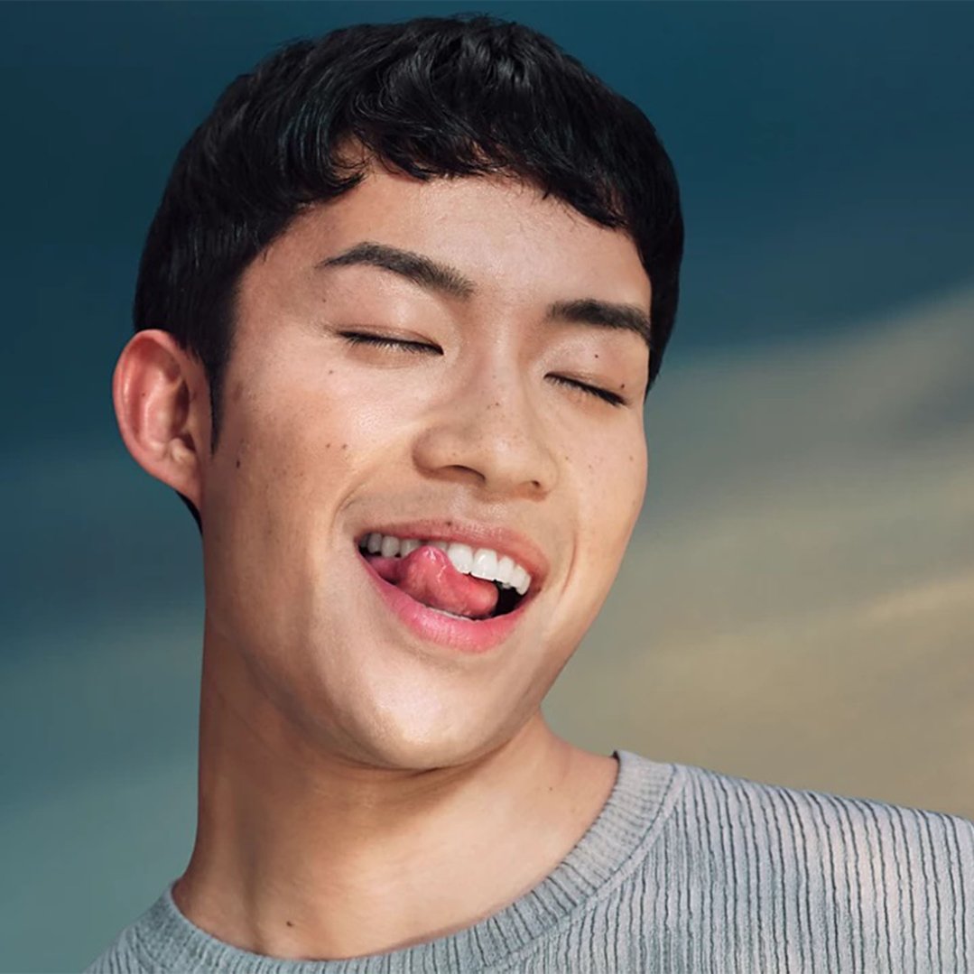 Man with eyes closed, licking his lips, wearing a grey sweater