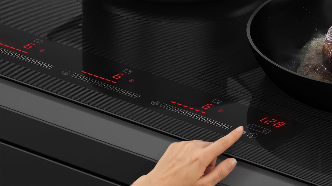 A hand adjusts the settings on a black induction cooktop with a pan cooking