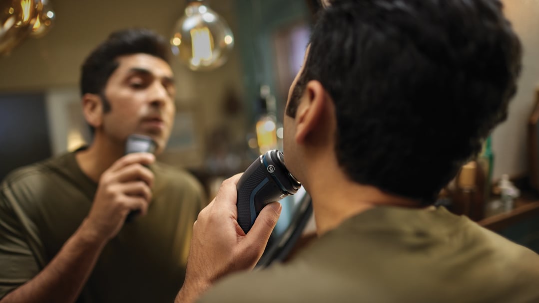 Man shaving with a Philips electric shaver in front of a mirror