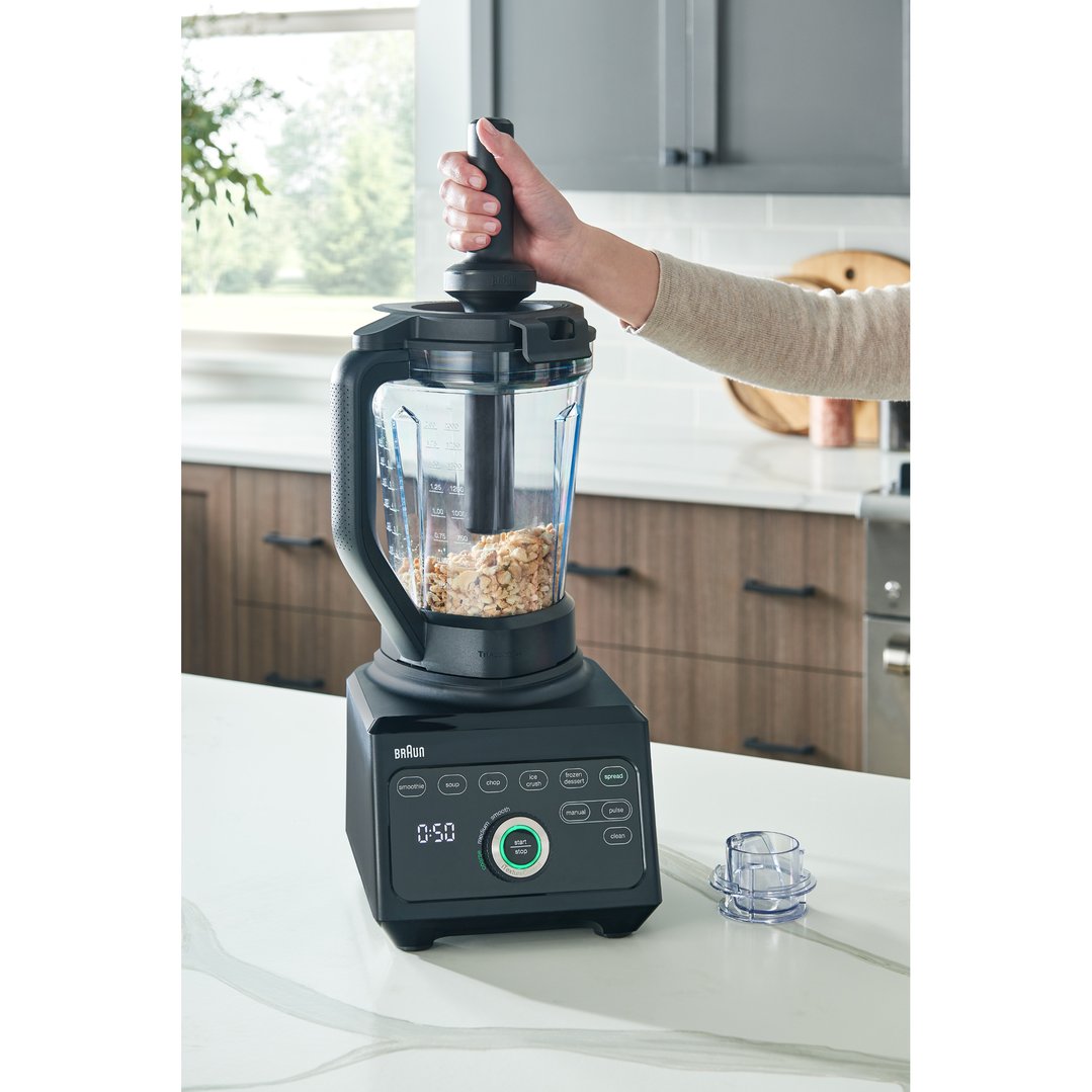 Hand holding tamper in a Braun PowerBlend 9 Jug Blender with nuts inside