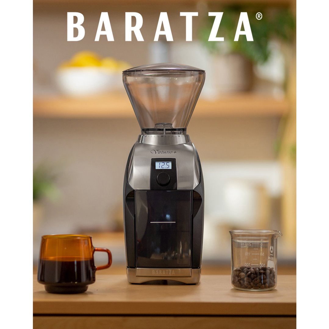 A Baratza Virtuoso+ coffee grinder on a wooden counter with a mug and coffee beans