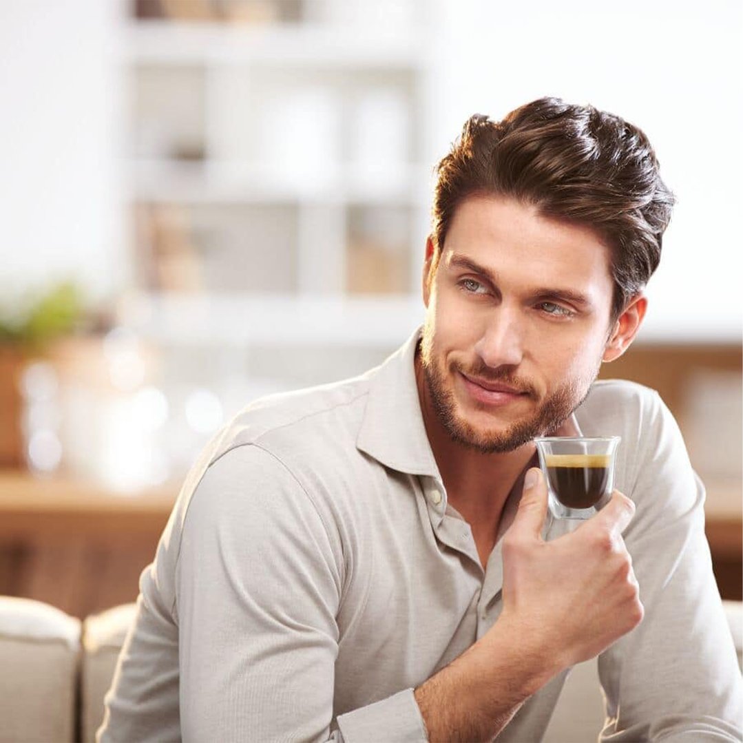 Man holding a small glass of espresso in a living room setting