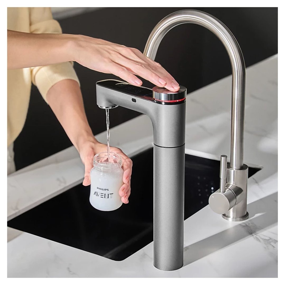 Woman's hand pressing button on a Philips water tap, filling a baby bottle