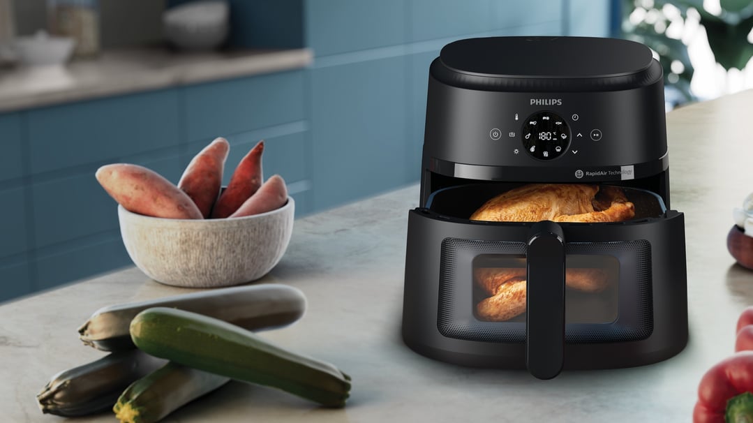 Black Philips airfryer cooking a whole chicken on a kitchen counter with vegetables