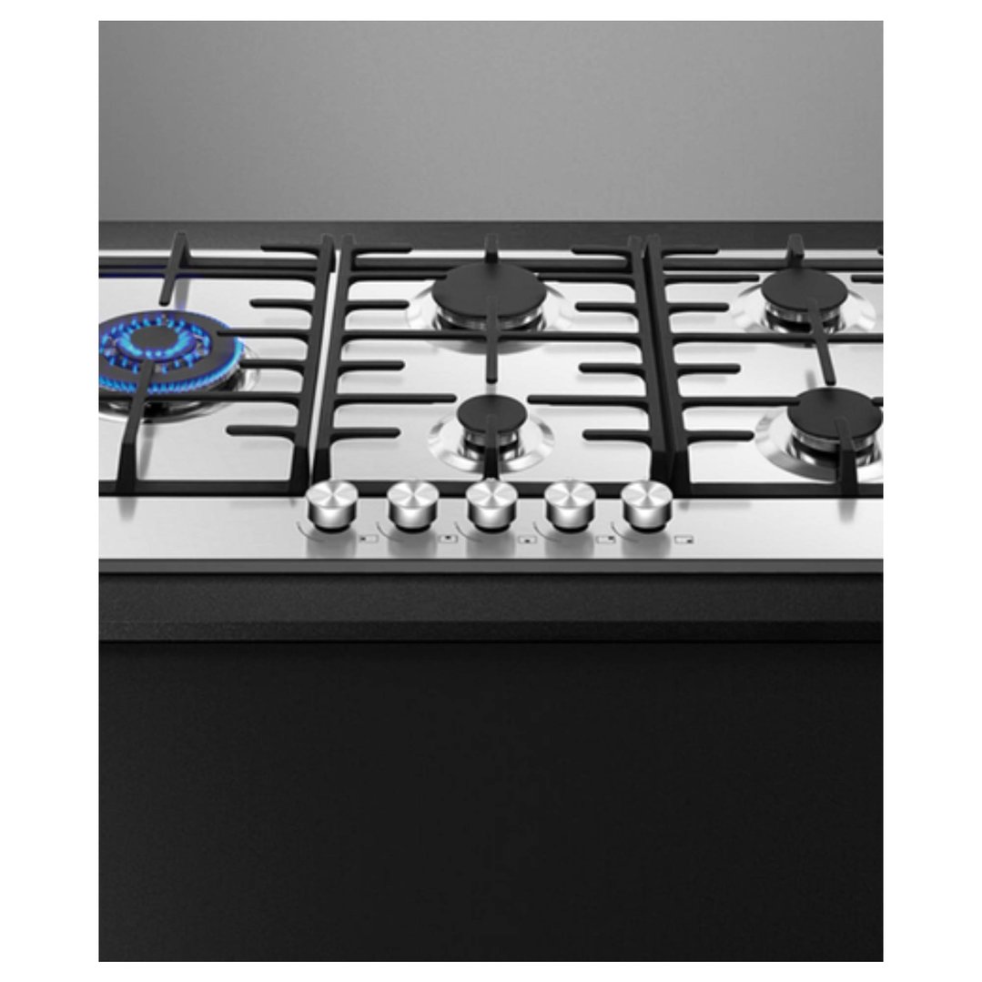 Stainless steel gas cooktop with five burners, one with blue flame, in a kitchen