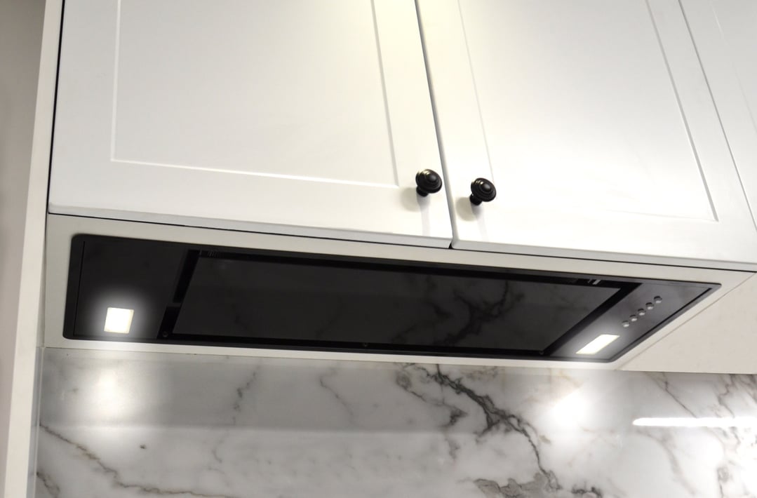 Black undermount rangehood installed under white kitchen cabinets with marble backsplash