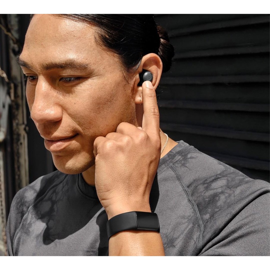 Man wearing a black smartWatch and earbud, touching the earbud