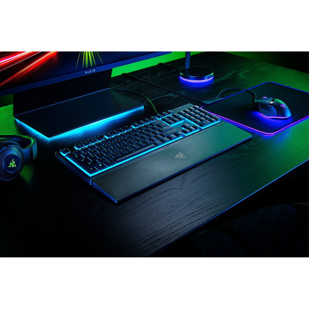 Razer gaming keyboard, mouse, and headphones on a dark desk with blue and green lighting
