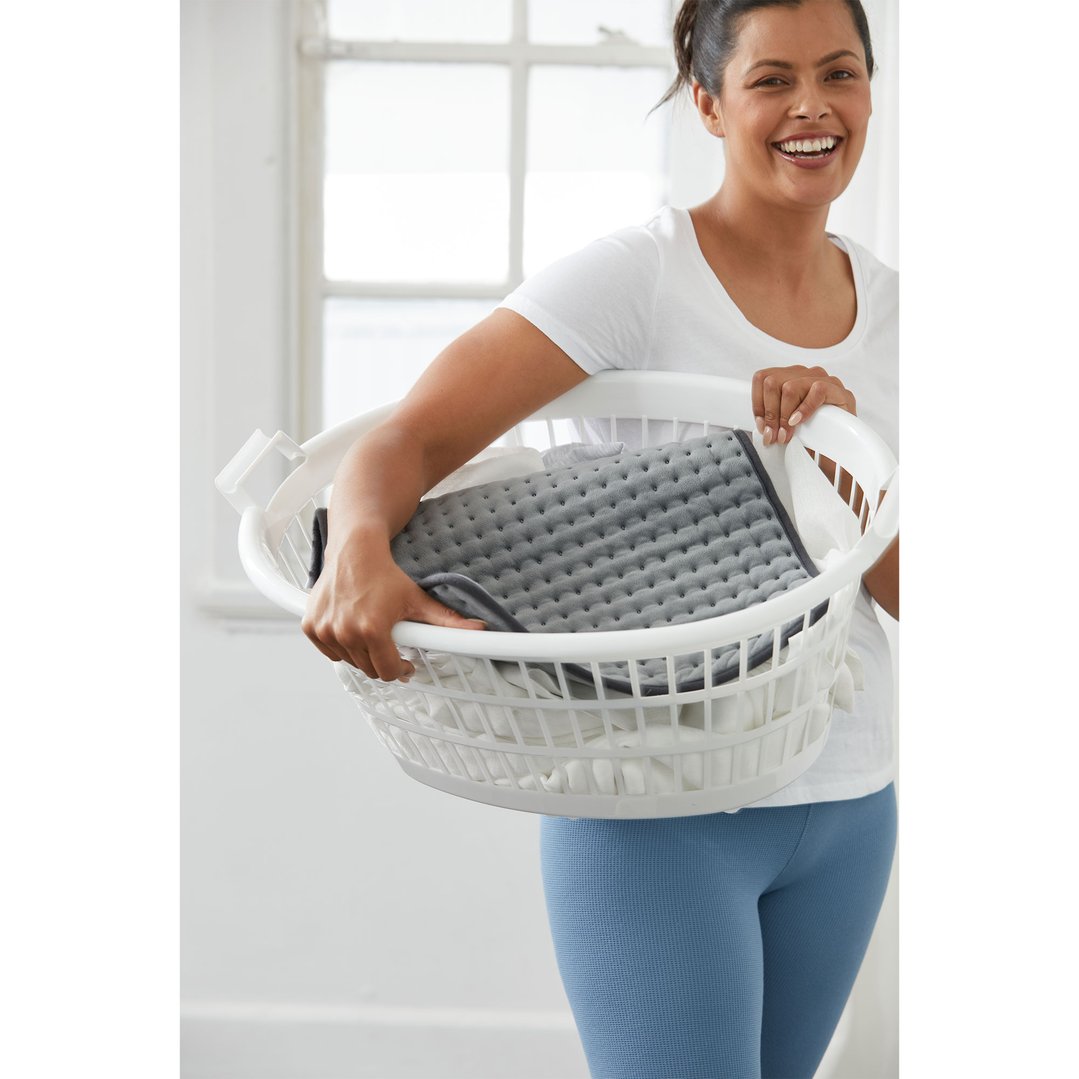 Woman holding a white laundry basket with a grey heating pad inside