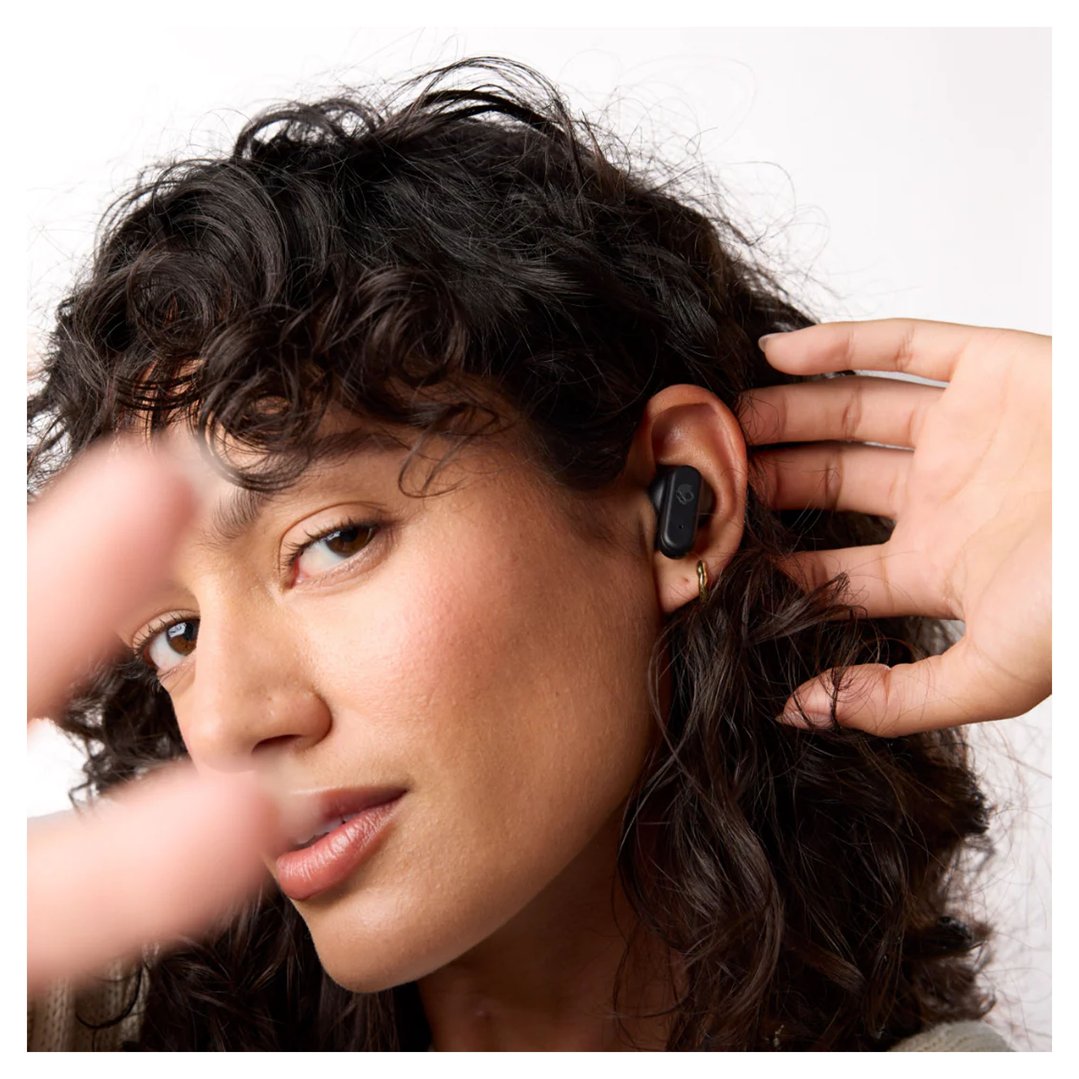 Woman with dark curly hair wearing a black Skullcandy earbud in her ear
