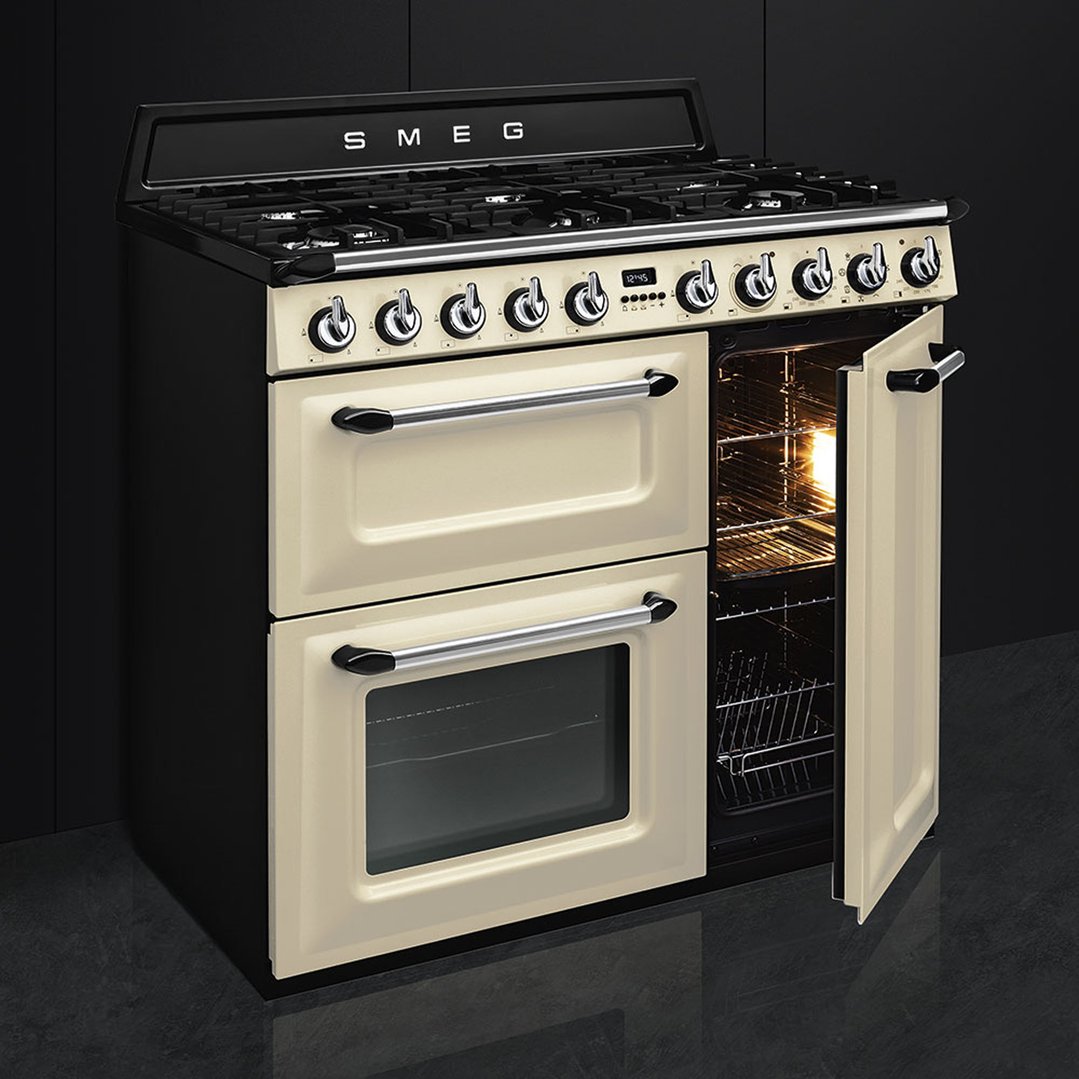 Cream freestanding cooker with one oven door open in a dark kitchen setting