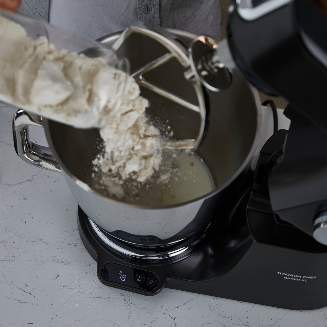 Hands pouring flour into a KENWOOD Titanium Chef Baker XL food mixer