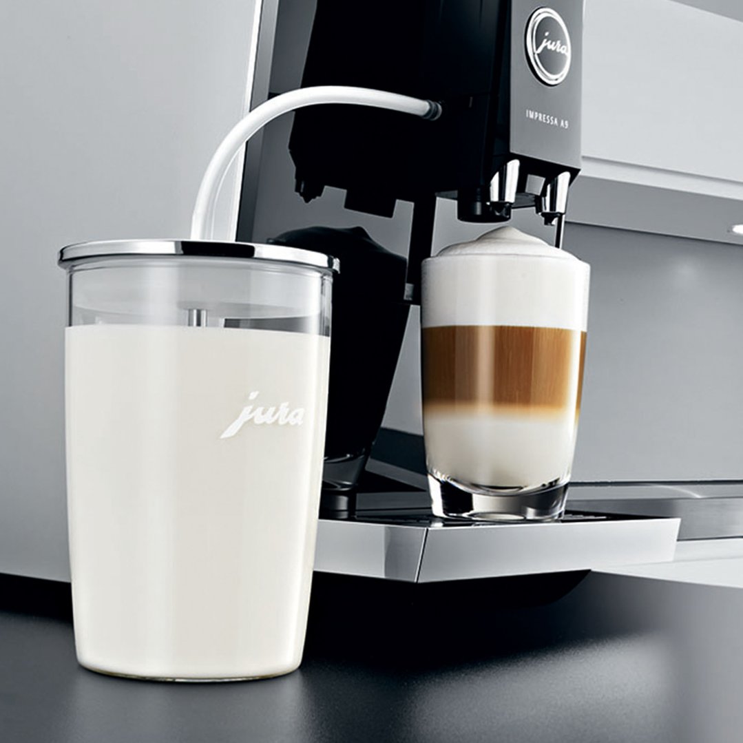 Glass milk container with milk next to a coffee machine making a latte