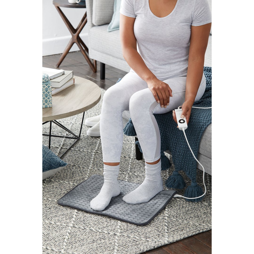 Woman sitting on a couch with her feet on a heating pad