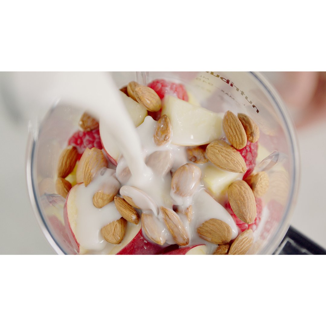 Milk being poured into a blender with fruit and almonds