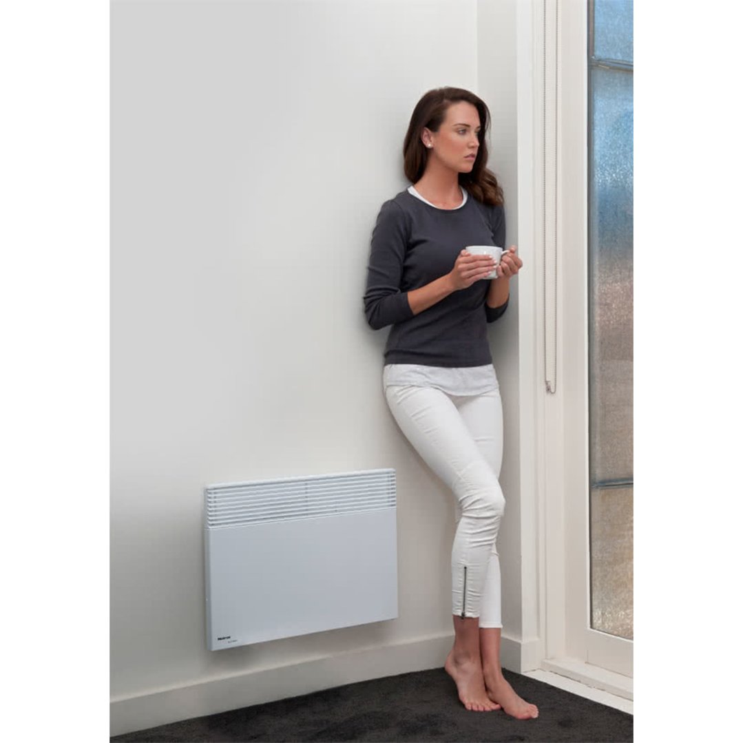 Woman holding a mug, standing next to a wall-mounted heater