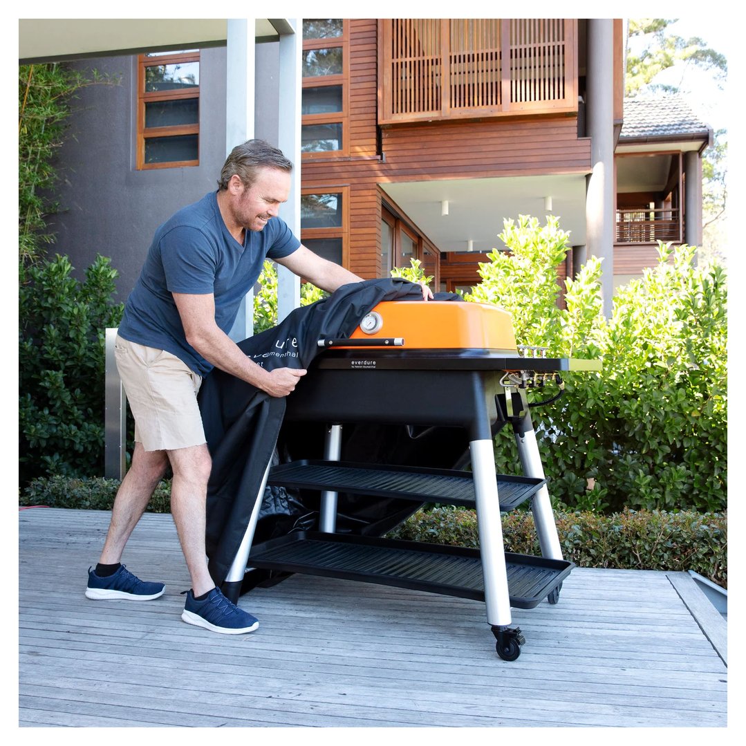 Man placing a black cover over an orange BBQ grill outdoors