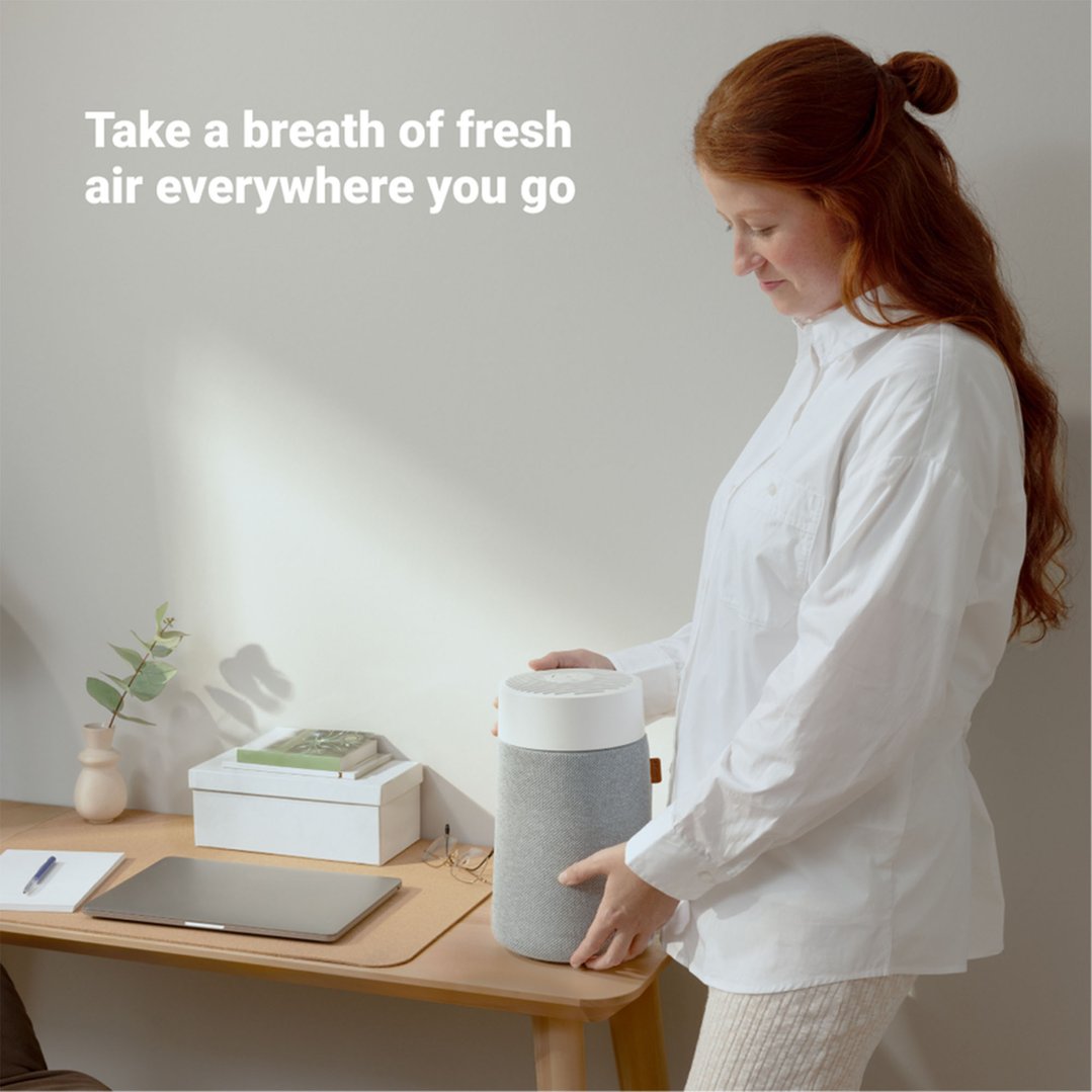Woman holding a Blueair Mini Air Purifier on a wooden desk