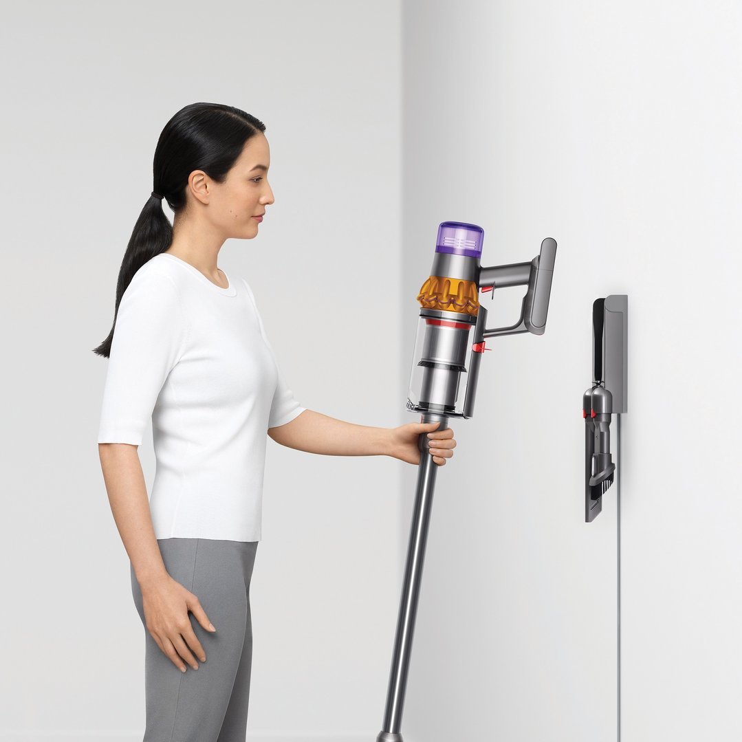 Woman holding a Dyson handstick vacuum next to a wall-mounted dock