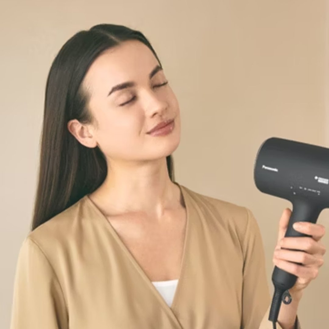Woman with closed eyes holding a black hair dryer to her hair