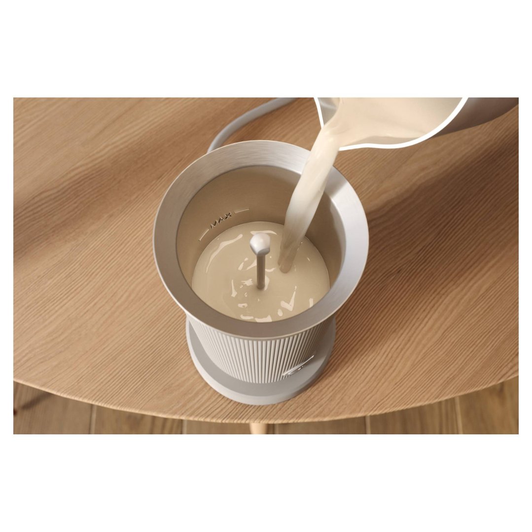 Milk being poured into a Baristina milk frother on a wooden table