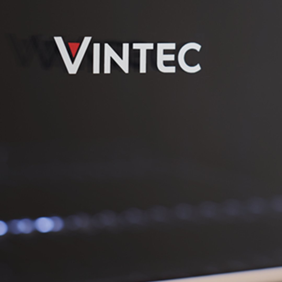 Close-up of the VINTEC brand logo on a dark background with blurred lights