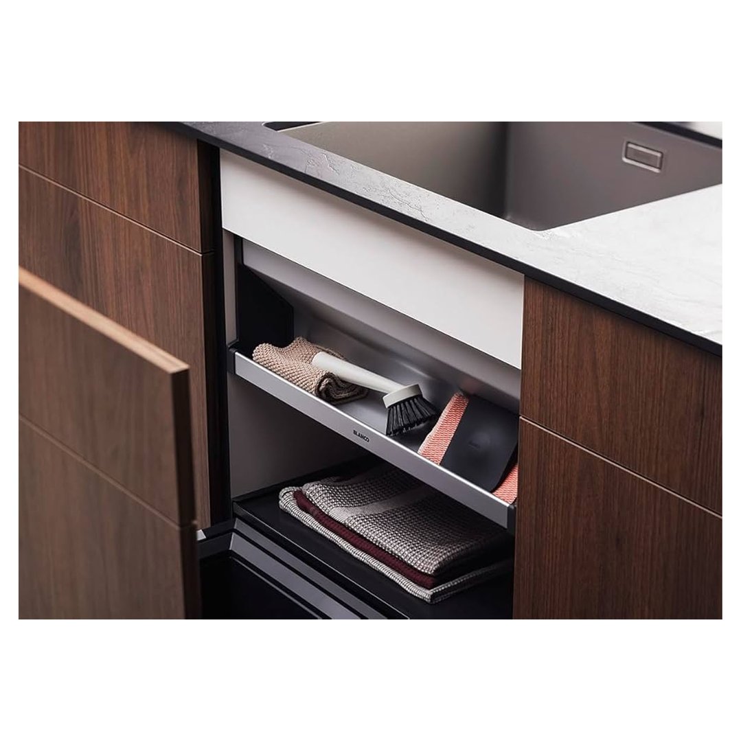 Open pull-out drawer under a sink with cleaning supplies and towels