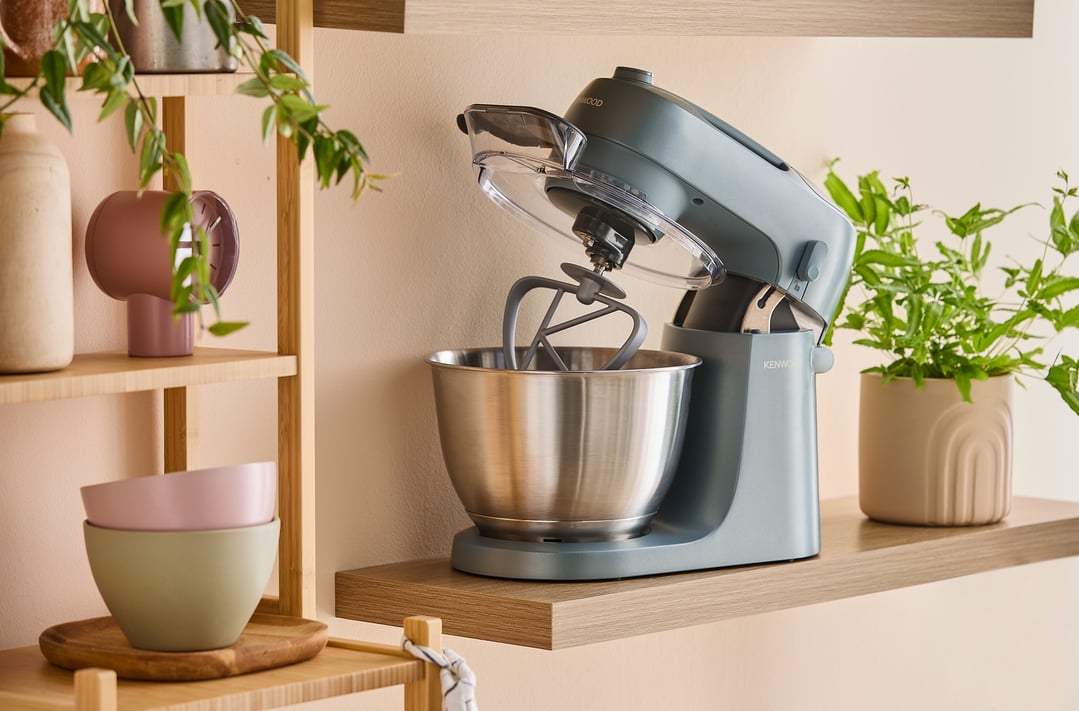 Blue Kenwood Go Stand Mixer on a wooden shelf with plants and bowls