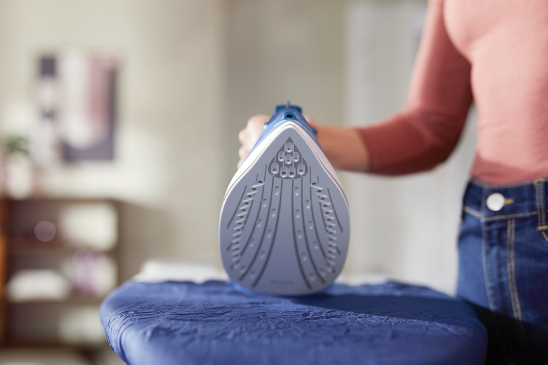 Person ironing blue fabric with a Philips steam iron on an ironing board