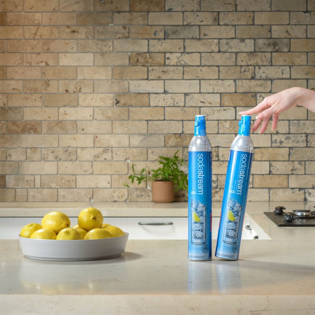 Hand reaching for a SodaStream gas cylinder on a kitchen counter with lemons