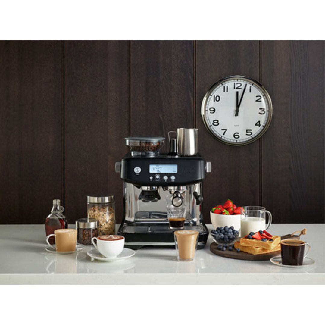 Black Breville coffee machine on a counter with breakfast items and a clock