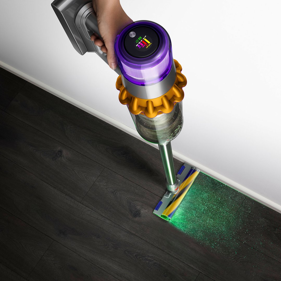 Hand holding a handStickVacuum, illuminating dust on a dark wooden floor