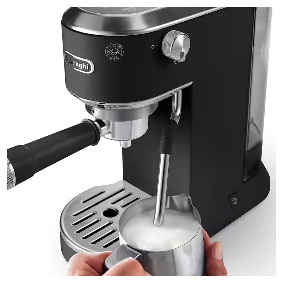 Hand holding a milk jug under the steam wand of a black coffee machine