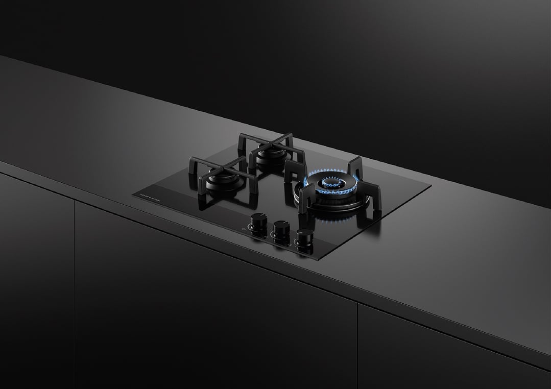 Black gas on glass cooktop with three burners, one lit, in a dark kitchen
