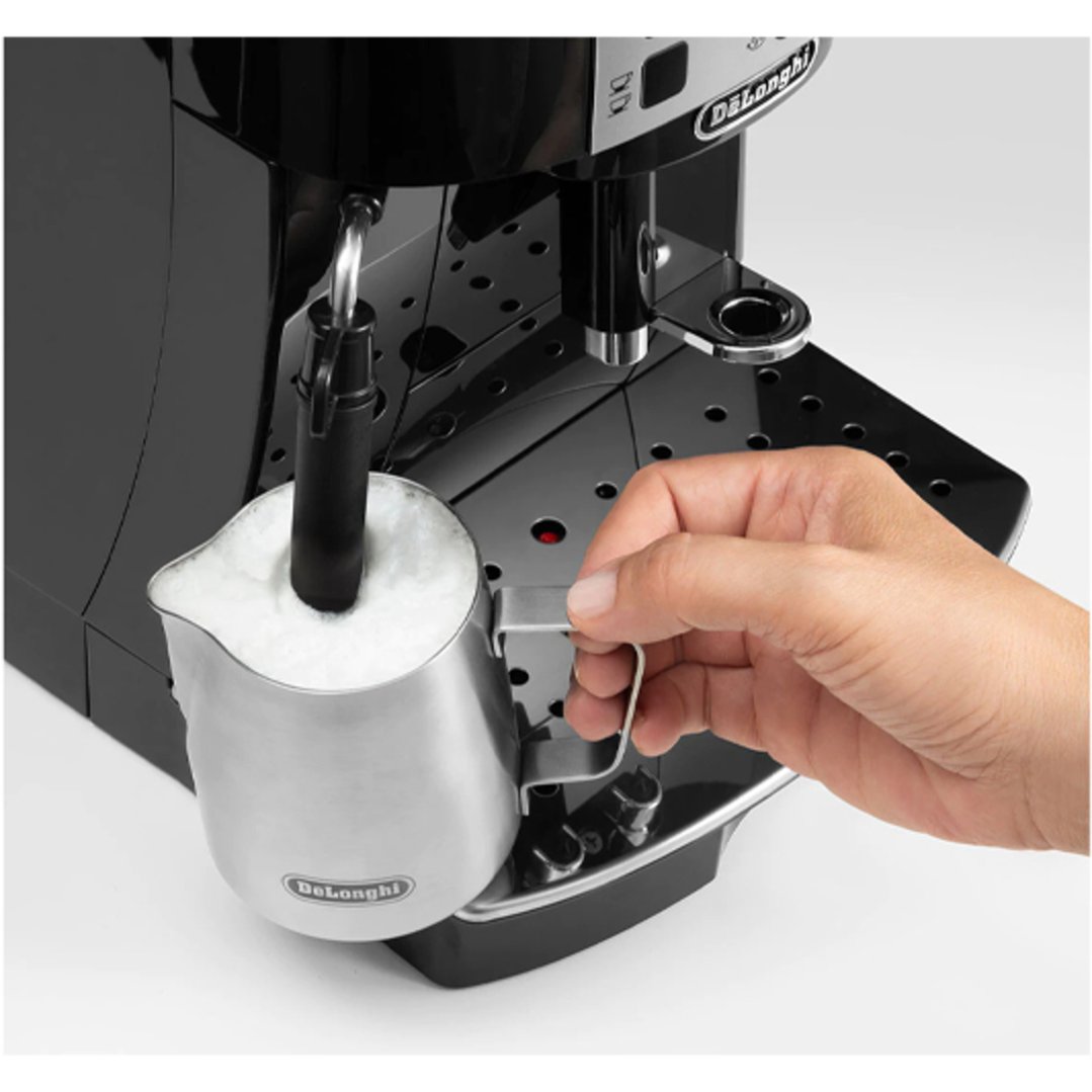 Hand holding a milk jug under the frother of a coffee machine
