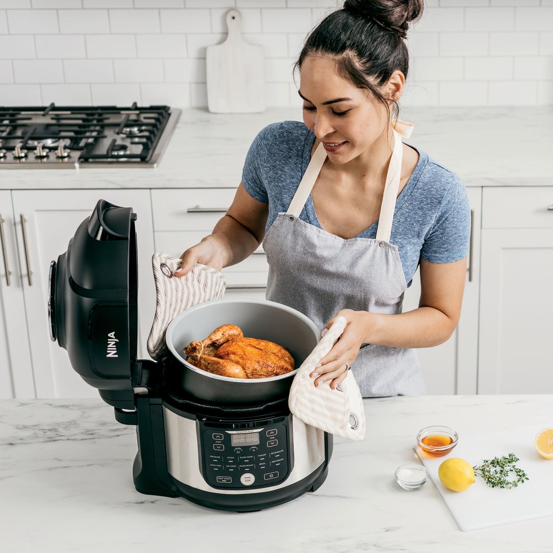 Woman removing a cooked chicken from a Ninja multi cooker in a kitchen