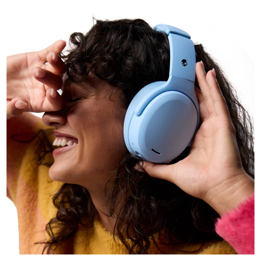 Woman wearing blue Skullcandy headphones, smiling with hands near her face