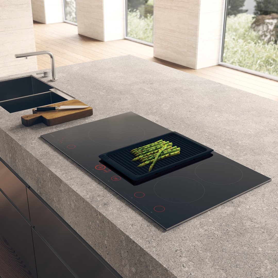 An induction hob cooktop with a grill pan of asparagus in a modern kitchen
