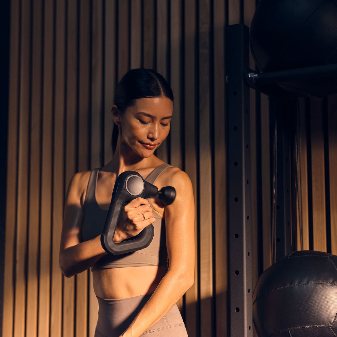 Woman using a black massager on her arm in a gym setting