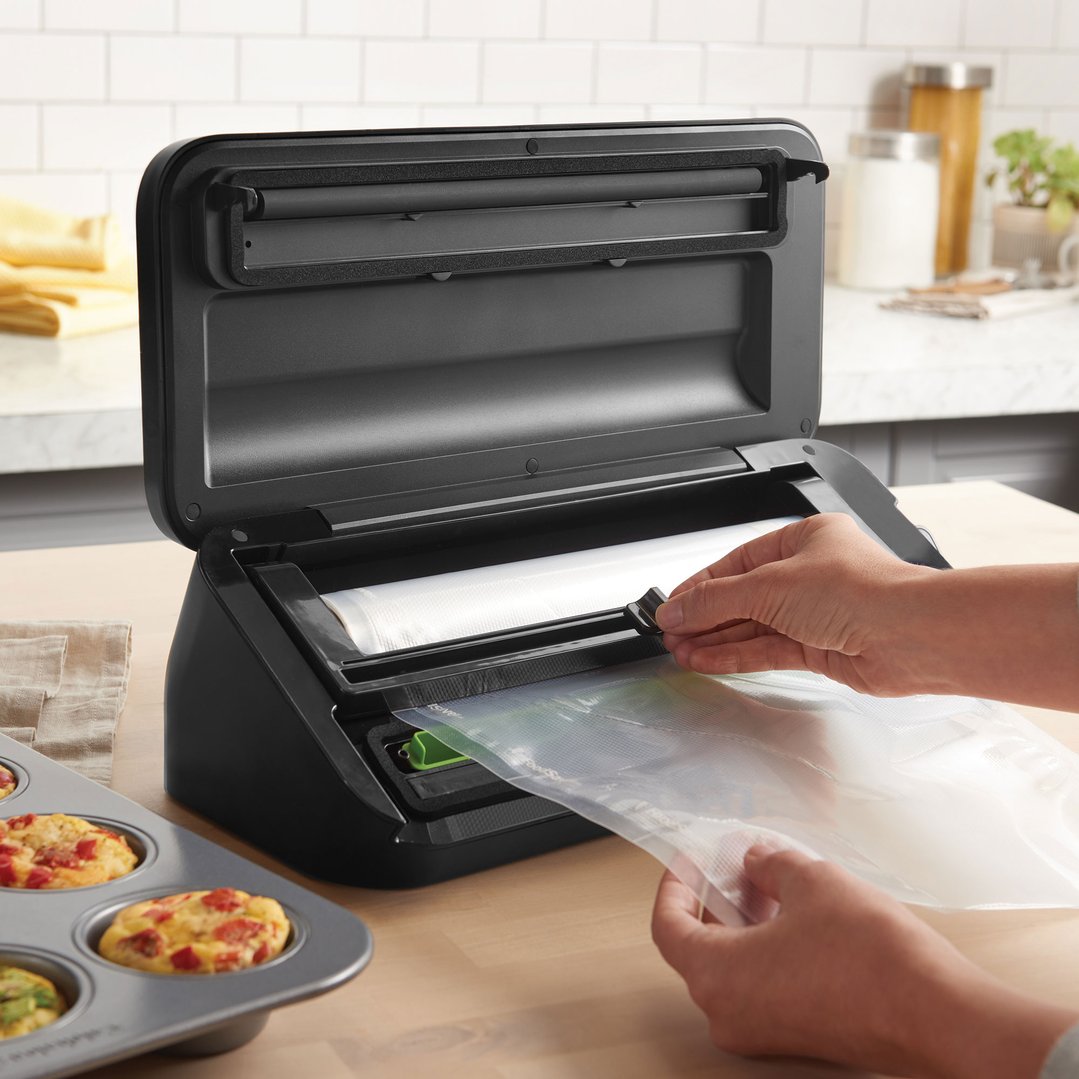 Hands using a black Sunbeam food vacuum sealer on a wooden kitchen counter