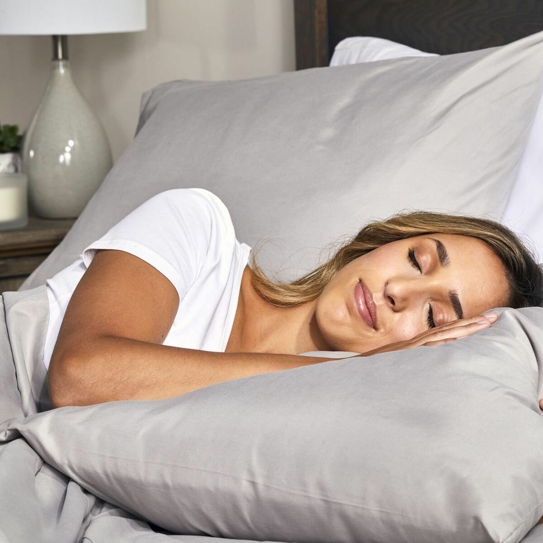 Woman sleeping on a bed with a grey pillow and bedding