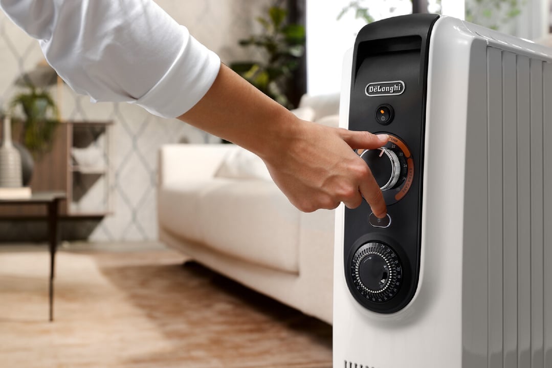 Hand adjusting settings on a white oil column heater in a living room
