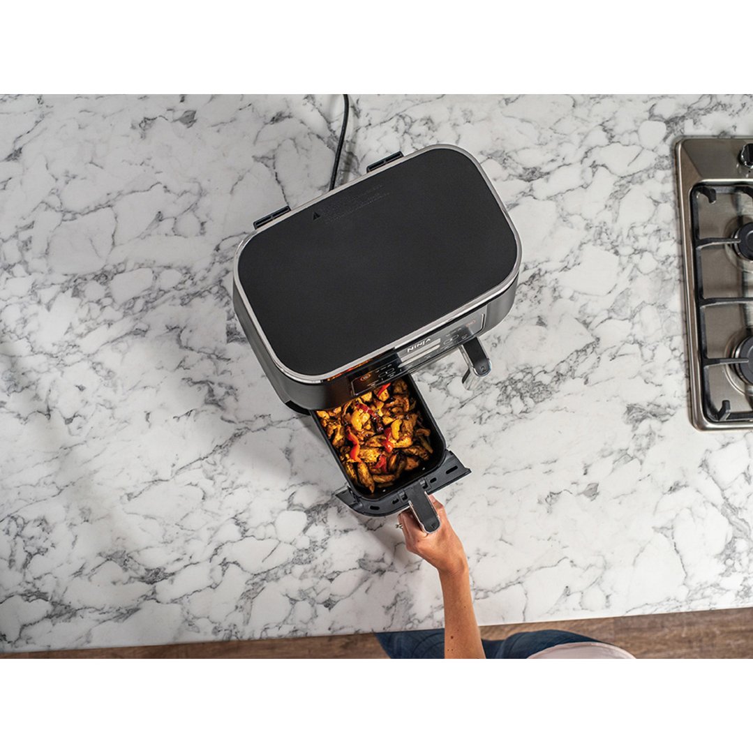 Person's hand pulling out a basket of food from a Ninja Foodi Dual Zone Air Fryer