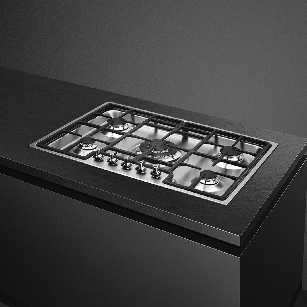 Stainless steel gas cooktop with five burners and control knobs built into a dark countertop