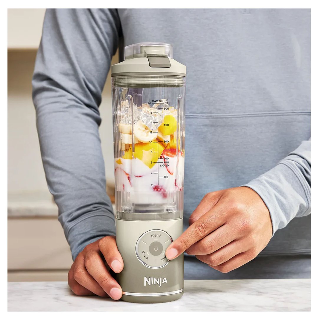 Person pressing the start button on a Ninja portable blender filled with fruit and yogurt