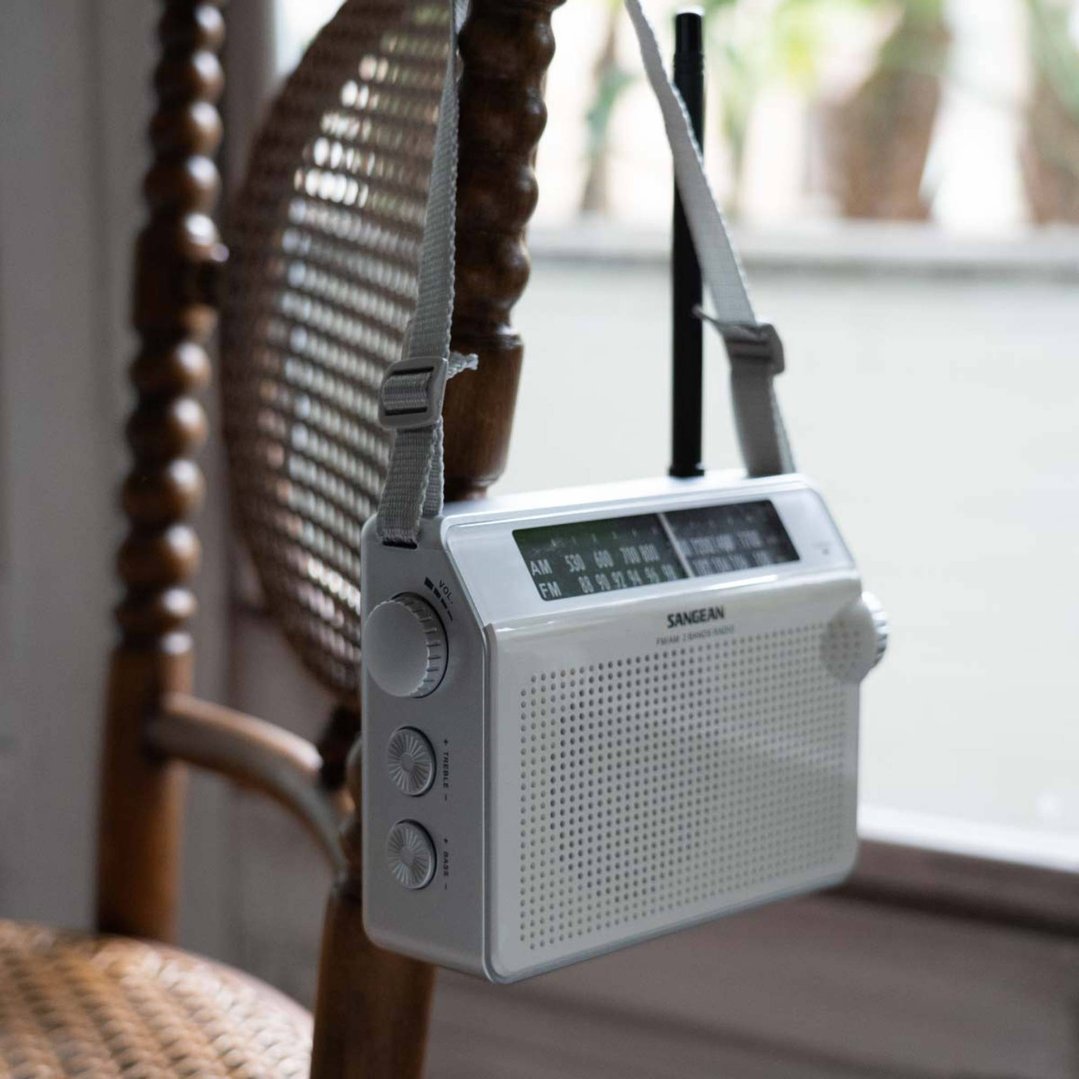 White portable radio with a strap hanging from a wooden chair indoors